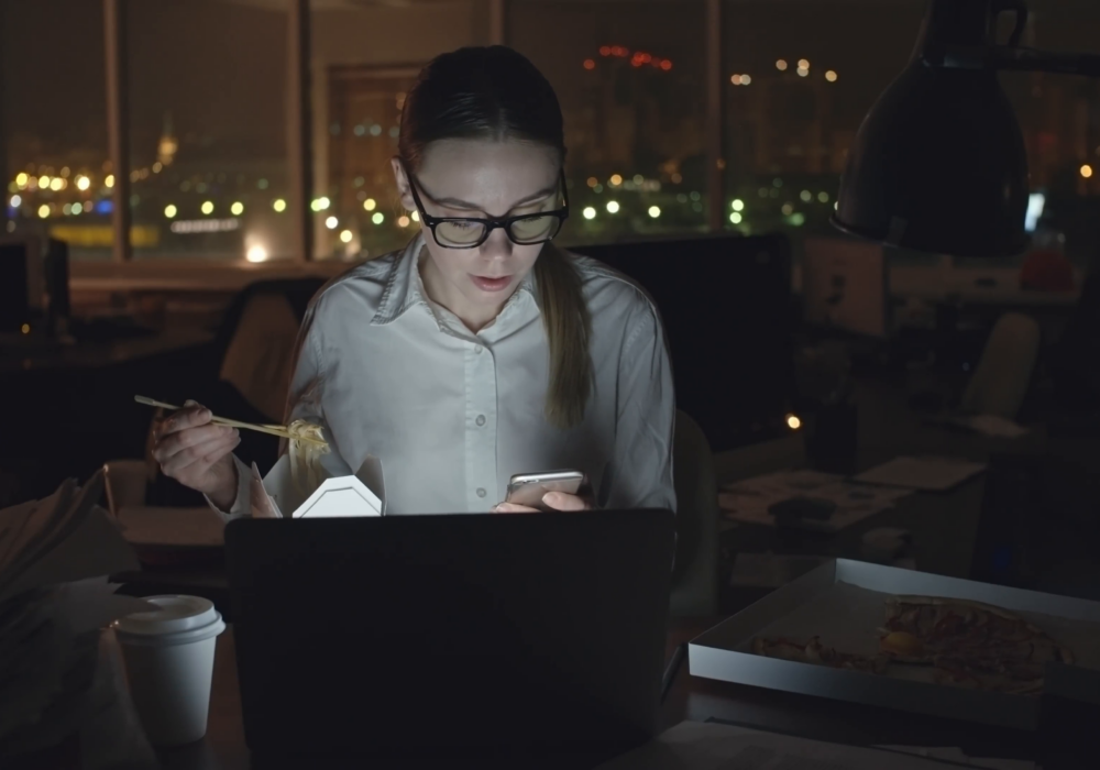 Young-businesswoman-sitting-at-desk-in-dark-office-working-on-laptop-talking-on-mobile-phone-and-eating-noodles-from-box-with-sticks-medium-shot-on-sony-nex700-odyssey-7q Rslnanugd