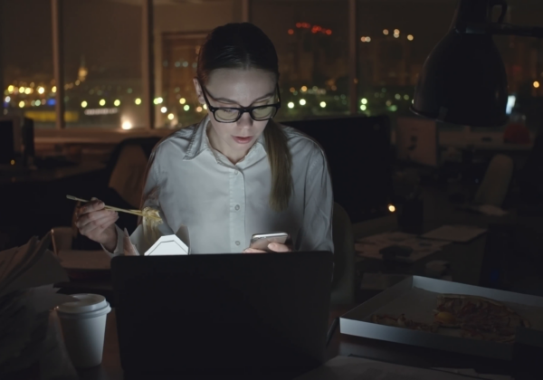 Young-businesswoman-sitting-at-desk-in-dark-office-working-on-laptop-talking-on-mobile-phone-and-eating-noodles-from-box-with-sticks-medium-shot-on-sony-nex700-odyssey-7q Rslnanugd 